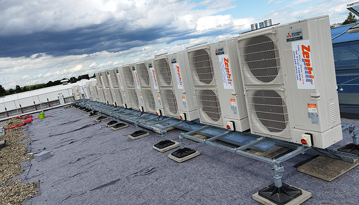 Auf einem Dach stehen mehrere Klimaanlagen in einer Reihe.