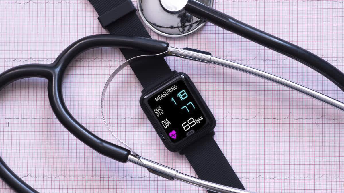 Eine Smartwatch liegt gemeinsam mit einem Stethoskop auf einem medizinischen Auswertungsblatt.