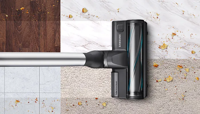 Ein Samsung-Staubsauger mit Rohr auf verschiedenen Oberflächen mit Krümeln, darunter Holz, Fliesen, Marmor und Teppich.