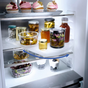 Ein Kühlschrank gefüllt mit Gläsern mit eingelegten Speisen, Desserts und Getränken auf mehreren Regalen.