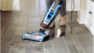 Ein Staubsauger mit Wischfunktion reinigt den Fliesenboden, auch welchem Krümel liegen. 