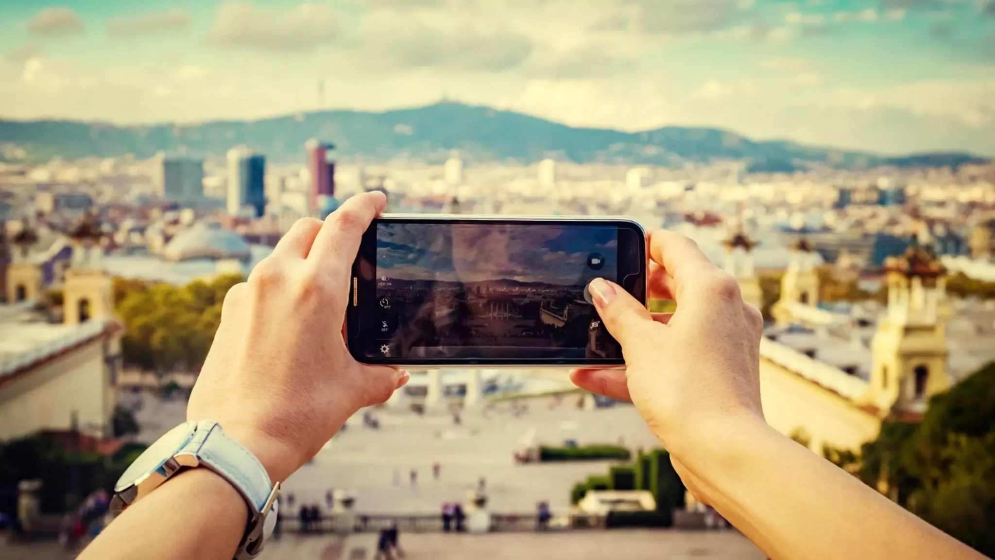 Eine Person knipst mit dem Handy ein Foto von der Skyline einer Stadt.