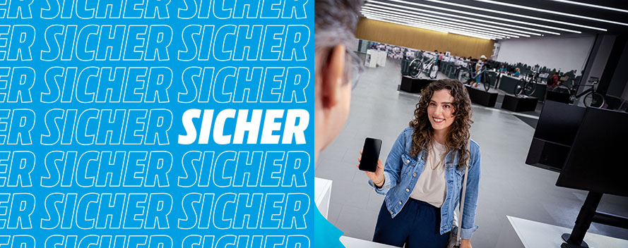 Eine Frau hält ein Smartphone in einem Fahrradgeschäft. Im Hintergrund stehen viele Fahrräder aufgereiht. Die Wand ist weiß.