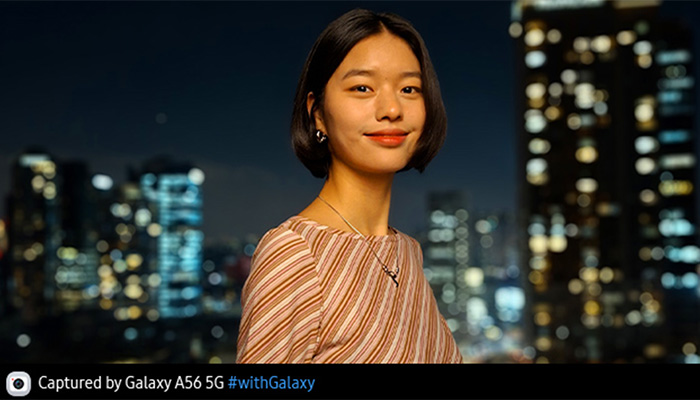 Eine Frau mit gestreiftem Oberteil steht vor einer unscharfen Stadtlandschaft bei Nacht. Sie trägt Ohrringe und eine Halskette.