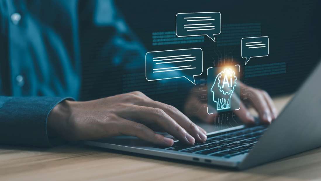 Eine Person tippt auf einem Laptop. Über dem Laptop sind Chatblasen und ein KI-Symbol zu sehen.