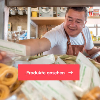 Verkäufer in einem kleinen Laden greift lächelnd nach verpackten Lebensmitteln; im Vordergrund ein Button mit der Aufschrift „Produkte ansehen“.