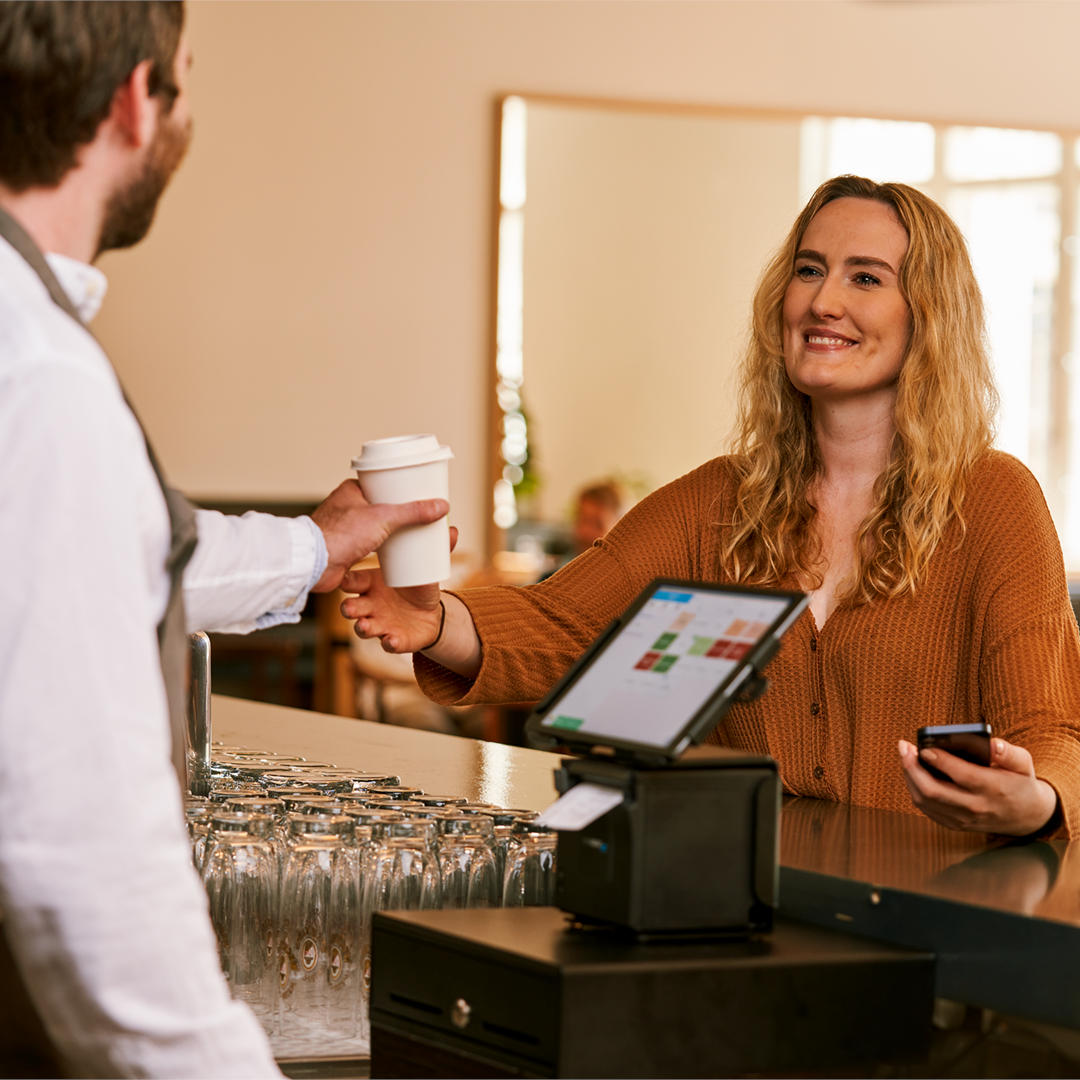 Eine Frau zahlt einen Kaffee mit ihrem Smartphone an der Kasse.