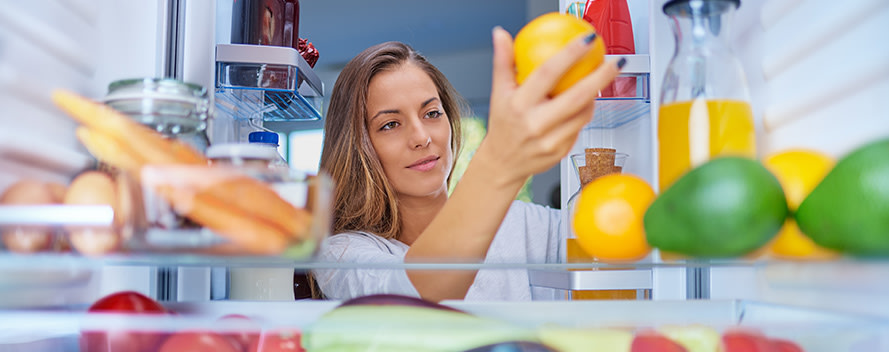 Eine Frau greift in einen Kühlschrank und holt eine Orange heraus.