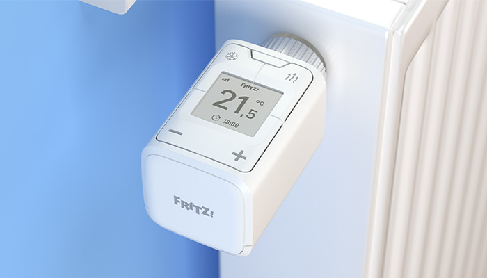 Ein weißer, digitaler Heizkörperthermostat zeigt 21,5 Grad Celsius an, montiert an einem Heizkörper vor einem blauen Hintergrund.