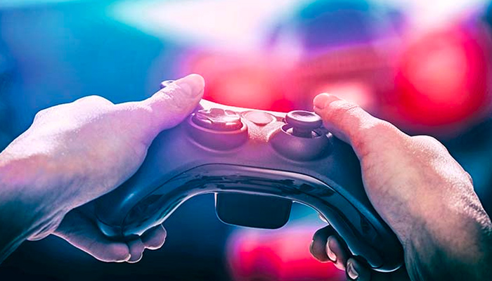 Ein Videospiel-Controller wird von zwei Händen gehalten, mit verschwommenen roten und blauen Lichtern im Hintergrund.