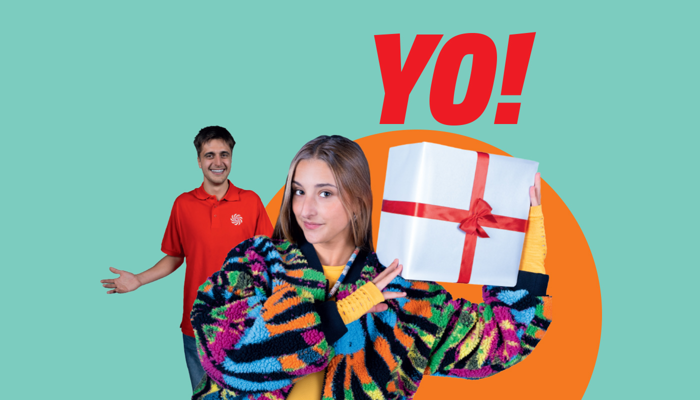 YO!“-Schriftzug auf türkisgrünem Hintergrund: vorne Kunde im bunten Pullover hält Geschenk mit roter Schleife, MediaMarkt-Mitarbeiter im Hintergrund.
