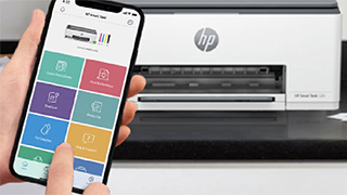 Ein Smartphone zeigt eine Drucker-App mit bunten Symbolen vor einem weißen HP-Drucker auf einer schwarzen Oberfläche.
