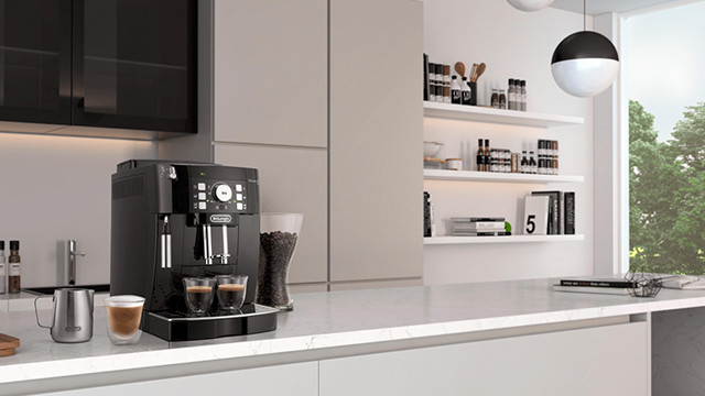 Eine schwarze Kaffeemaschine steht auf einer weißen Küchentheke mit Tassen, einem Krug und Regalen im Hintergrund.