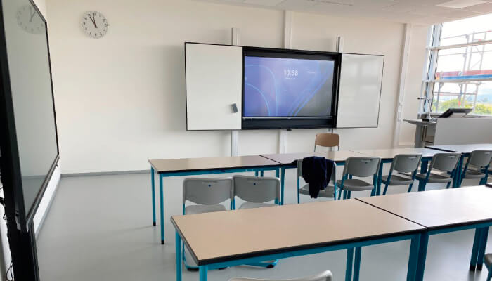 Ein Klassenzimmer mit Tischen, Stühlen und einer interaktiven Tafel an der Wand.