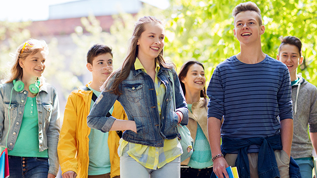 Eine Gruppe von sechs Jugendlichen geht im Freien, einige lächeln, gekleidet in Jacken und Pullover.