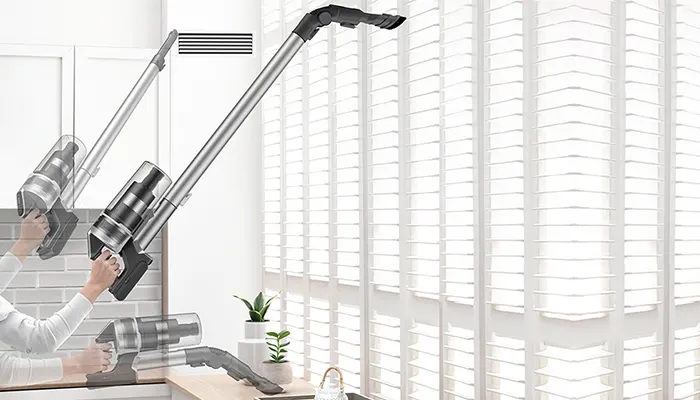 Ein silberfarbener Staubsauger wird vor einem Fenster mit weißen Jalousien und einer Pflanze auf dem Tisch gezeigt.