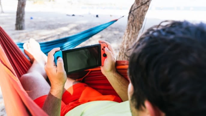 Ein Mann spielt mit einer Nintendo Switch Konsole in einer Hängematte.