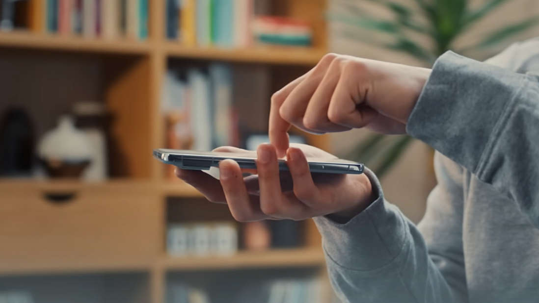 Eine Person tippt auf ein Smartphone vor einem Bücherregal.