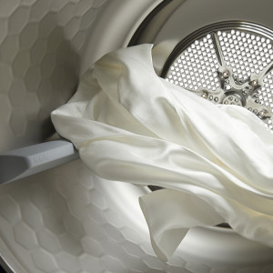 Weiße Stoffe liegen in einer silbernen Waschmaschine mit einer grauen Gummidichtung und einem perforierten Metalleinsatz.