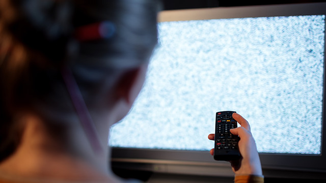 Eine Person hält eine schwarze Fernbedienung vor einem Fernsehbildschirm mit statischem Rauschen.