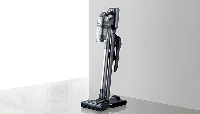 Ein grauer Staubsauger steht auf einer grauen Oberfläche vor einem hellen Hintergrund.