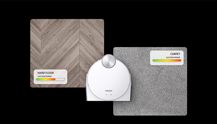 Ein weißer Roboterstaubsauger zwischen Holzbodenmuster und einem Teppichmuster auf schwarzem Hintergrund. Saugkraftanzeigen sind sichtbar.