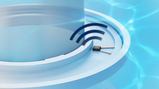 Ein Sensor liegt auf einer weißen, runden Oberfläche. Drei blaue, bogenförmige Linien darüber symbolisieren ein Signal. Im Hintergrund ist blaues Wasser zu sehen.