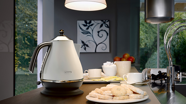 Ein Tisch mit Gebäck, Teetassen und einem weißen Wasserkocher in einer Küche mit Blick auf einen Garten durch ein Fenster.