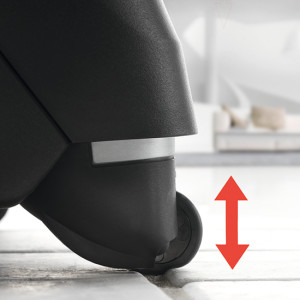 Schwarzes Gerät mit Rollen auf Bodenfliesen, daneben ein roter Pfeil, der vertikale Bewegung andeutet.