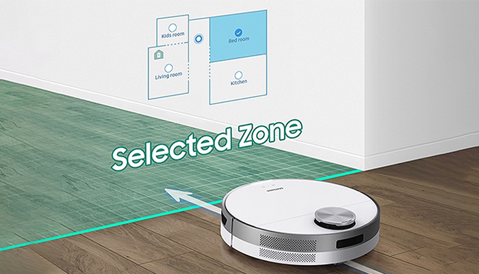 Ein weißer Saugroboter auf Holzboden, neben einer Wand mit Raumplan und dem Text "Selected Zone".