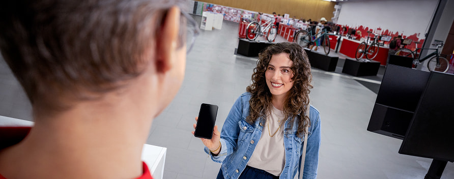 Eine Frau zeigt ein Smartphone einem Mitarbeiter in einem Geschäft