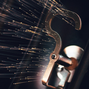 Metallischer Haken mit leuchtenden Fäden vor dunklem Hintergrund, Fokus auf Detail und Textur.