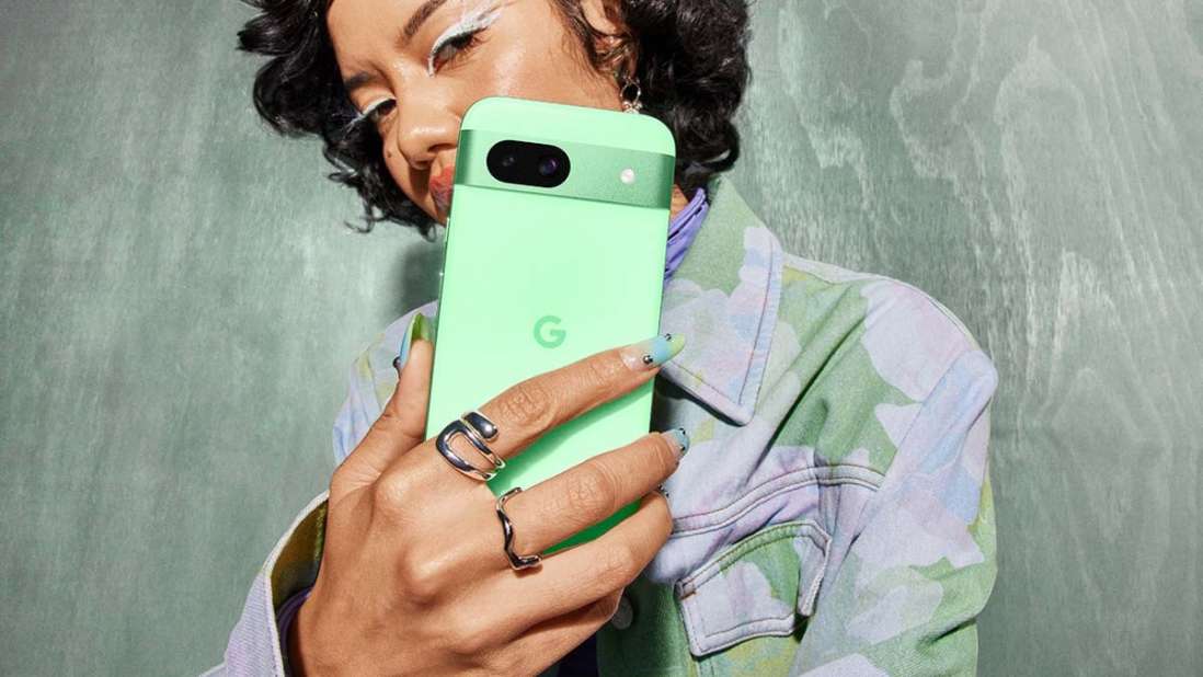 Eine Person hält ein hellgrünes Smartphone mit silbernem "G"-Logo vor einem strukturierten, farblich passenden Hintergrund.