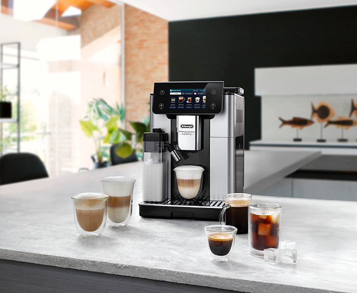 Auf einer Küchentheke steht eine Kaffeemaschine neben zwei Tassen Kaffee. Eine Schale Müsli und rote Johannisbeeren stehen davor.