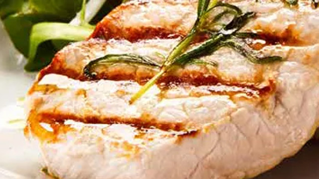 Ein gegrilltes Hähnchenbrustfilet mit Rosmarin und Salat wird auf einem Teller serviert.