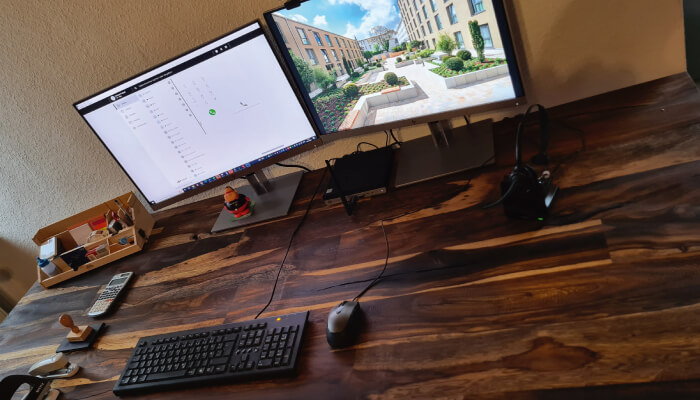 Zwei Monitore auf einem Schreibtisch mit Tastatur, Maus und Headset.