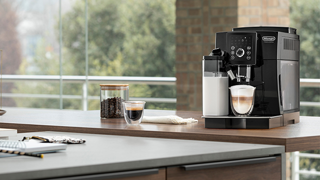 Auf einer Küchentheke stehen eine Kaffeemaschine, ein Glas Kaffee, ein Glas und eine Tasse Espresso.