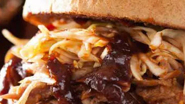 Nahaufnahme eines Sandwiches mit Fleisch, Krautsalat und dunkler Soße zwischen zwei hellen Brötchenhälften.