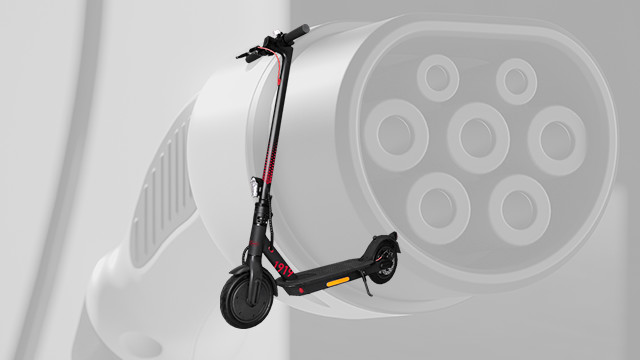 Ein schwarzer Elektroroller steht vor einem unscharfen, weißen Ladestecker mit runden Öffnungen.