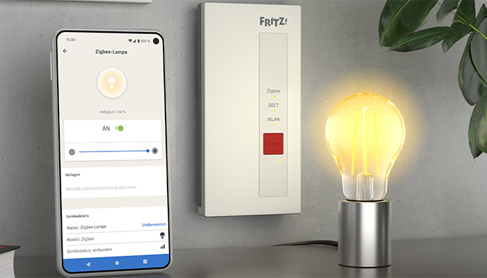 Ein Smartphone zeigt eine App zur Steuerung einer Glühbirne neben einer FRITZ!Box und einer leuchtenden Glühbirne.