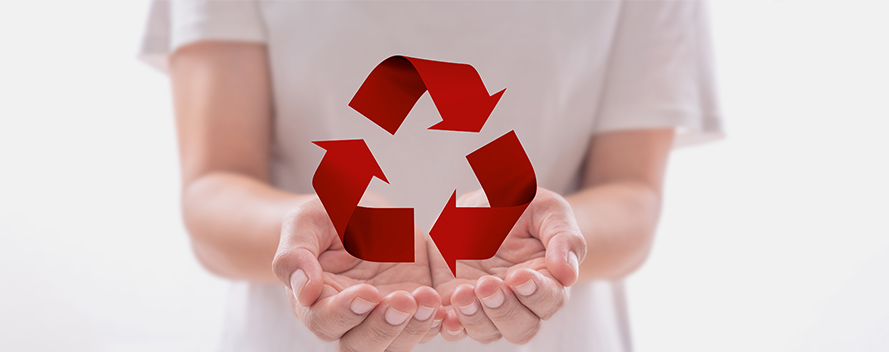 Eine Person im weißen T-Shirt hält ein rotes Recycling-Symbol in ihren Händen vor einem hellen Hintergrund.