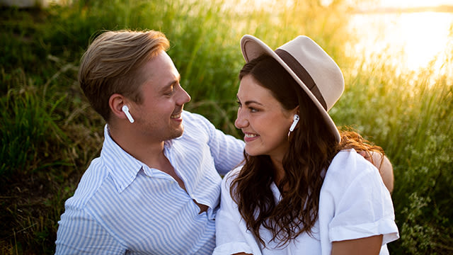 Ein Paar sitzt im Grünen und haben jeweils einen In-Ear-Kopfhörer im Ohr.