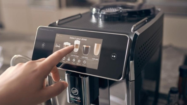 Eine Hand berührt den Bildschirm einer schwarzen Kaffeemaschine, um ein Getränk auszuwählen.