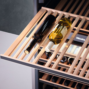 Auf einem Holzregal liegen zwei Weinflaschen, eine dunkel, eine hell, in einem Weinkühlschrank.