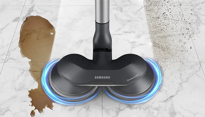 Ein grauer Samsung-Staubsauger reinigt braune Flecken und Staub auf einem weißen Marmorboden.