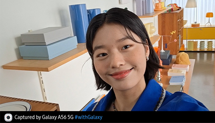 Eine Person macht ein Selfie in einem Raum mit Regalen. Die Regale sind mit blauen und grauen Kisten gefüllt. Im Hintergrund ist ein gelber Schrank zu sehen.