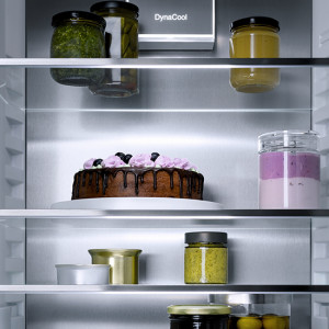 Ein Kühlschrank mit Glasböden, gefüllt mit Gläsern, einem Kuchen und Zitronen.