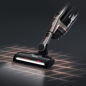 Ein kabelloser Staubsauger in Silber und Schwarz steht auf einem Rastermuster, das von unten beleuchtet wird.