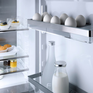 Im Kühlschrank: Glasböden mit Eiern, Flaschen und Schalen mit Speisen. Helle Innenbeleuchtung.