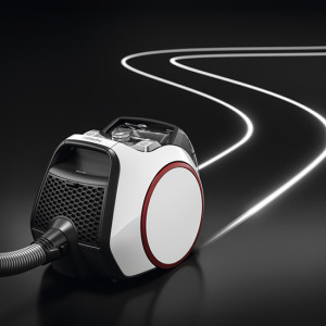 Ein weißer Staubsauger mit roten Akzenten steht auf einem schwarzen Untergrund, der eine geschwungene, leuchtende Linie hinterlässt.